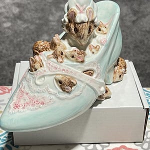 May include: A white ceramic mug with a black handle and the text "But First, Coffee" in a bold, black font. The mug is set against a blurred background, suggesting a cozy setting.