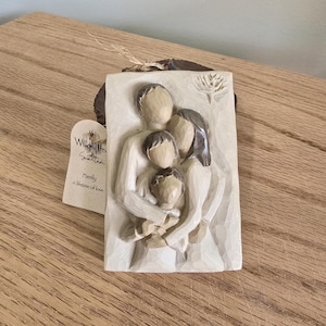 May include: A cream-colored relief sculpture of a family of four, embracing. The sculpture is rectangular and features a mother, father, and two children. The tag reads "Family A lifetime of love."