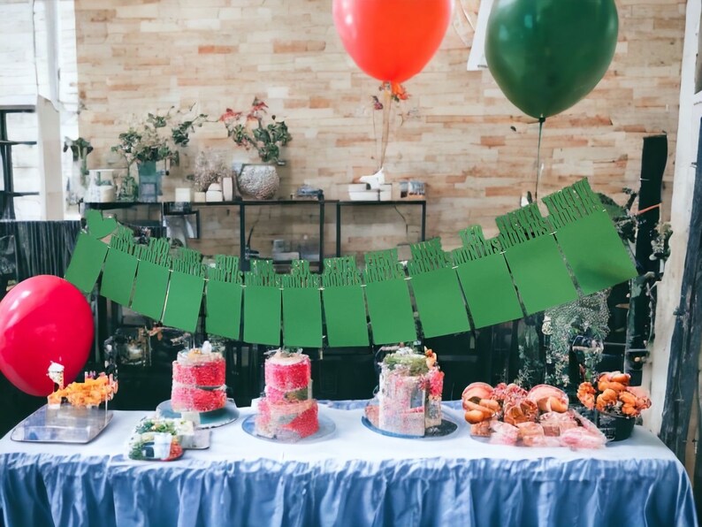 May include: A table with a blue tablecloth is set with three pink and white layered cakes, a bowl of fruit, and a green banner with the text "Happy Birthday". There are also two balloons, one red and one green.