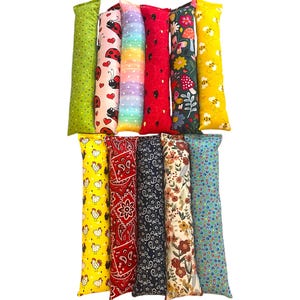 May include: Eleven rectangular fabric tubes arranged in two rows. The patterns include green with dots, ladybugs and hearts, rainbow ombre, red with black spots, floral with mushrooms, yellow with bees, yellow with chickens, red paisley, navy paisley, floral, and blue dots.