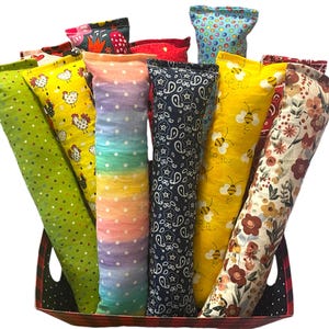 May include: A collection of long, cylindrical fabric pouches in a variety of patterns and colors, including green with dots, yellow with chickens, rainbow with white dots, navy blue with paisley, yellow with bees, and floral prints in a basket.