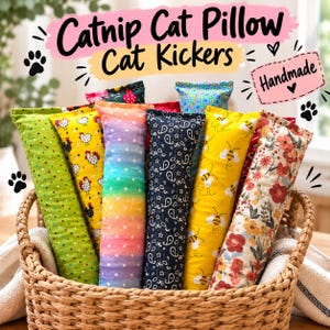 May include: A collection of rectangular catnip cat kicker pillows in a woven basket. The pillows feature various patterns including green polka dots, yellow chickens, rainbow gradients, black paisley, yellow bees, and red floral prints with text.