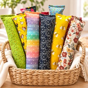 May include: A collection of rectangular fabric pouches in a woven basket. The pouches feature various patterns including green with polka dots, yellow with chickens, a rainbow gradient with white dots, navy blue paisley, yellow with bees, and floral prints.