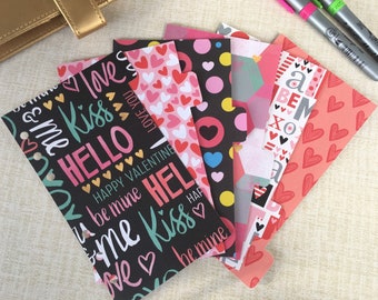 May include: A set of six Valentine's Day themed planner dividers with different patterns and colors. The dividers feature hearts, polka dots, and text such as "Kiss Me" and "Happy Valentine".