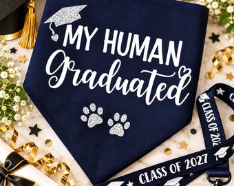 May include: A navy blue triangular pet bandana featuring the white text "MY HUMAN Graduated" with a silver glitter graduation cap and two silver glitter paw prints. Accompanying the bandana is a navy blue lanyard with "CLASS OF 2027" printed in white.