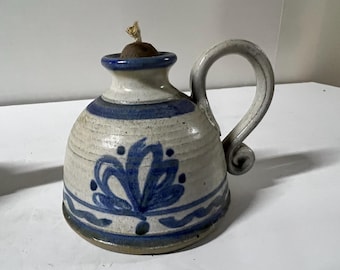 May include: A white ceramic oil lamp with a blue and white floral design. The lamp has a handle and a spout for pouring oil.