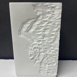 Może przedstawiać: Biały wazon z porcelany z wypukłym, fakturowanym wzorem. Wzór przedstawia stylizowaną  kwiat i abstrakcyjne linie.