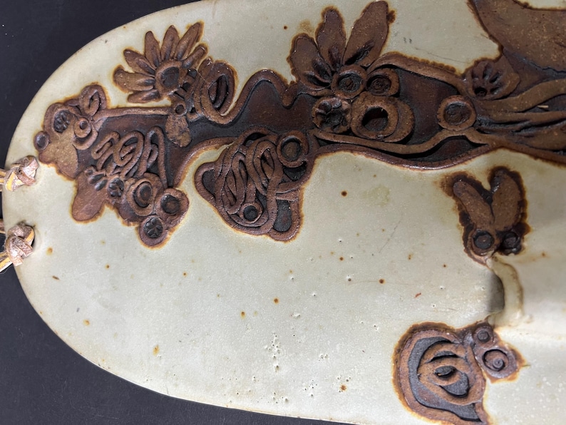 May include: A white ceramic plate with a brown floral design. The design features intricate swirls and loops, creating a unique and artistic pattern.