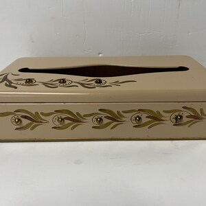 Op de afbeelding: Een beige metalen tissueboxhoes met een bloemenpatroon en gouden accenten. De doos heeft een gleuf om tissues uit te trekken.