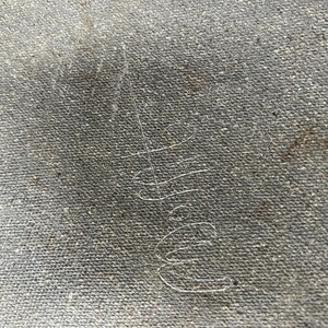 May include: Close-up of a grey canvas texture with a faint, handwritten signature in white ink.