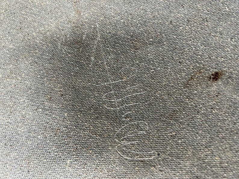 May include: Close-up of a grey canvas texture with a faint, handwritten signature in white ink.