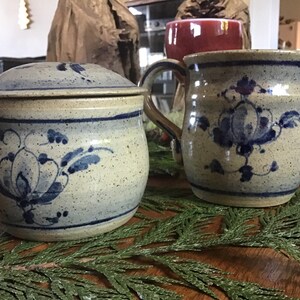 May include: A set of two ceramic kitchenware pieces with blue and white floral designs. The pieces are a covered jar and a pitcher.