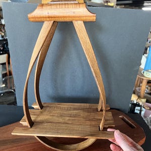 May include: A handcrafted wooden serving tray with a unique design. The tray features a rectangular base with curved supports and a handle. The wood has a warm, natural finish, showcasing the grain. The tray is designed for serving food or displaying items.
