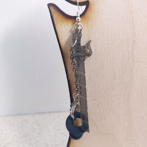 May include: A pair of earrings featuring a silver chain and a black sword charm with a blue ring charm hanging from the chain.