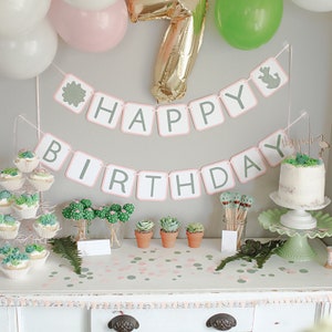 May include: A green and pink cactus themed birthday party with a banner that says "Happy Birthday". The table is decorated with green and pink confetti, cupcakes, and cactus cake pops.