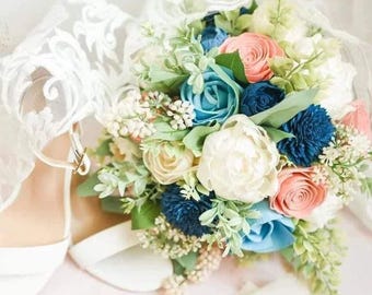 May include: A bridal bouquet with white, peach, and blue flowers. The bouquet is wrapped in white lace and features a variety of flowers, including roses, peonies, and hydrangeas.