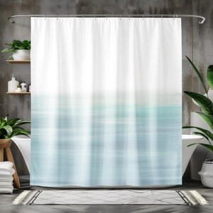 May include: White shower curtain with a blurred, abstract design in shades of blue and teal. The top portion is solid white, transitioning to a horizontal striped pattern. The curtain hangs from a silver rod, creating a modern bathroom aesthetic.