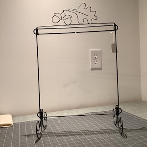 May include: Black metal stand with an acorn and oak leaf design. The stand has two shelves and a decorative scroll design at the base.