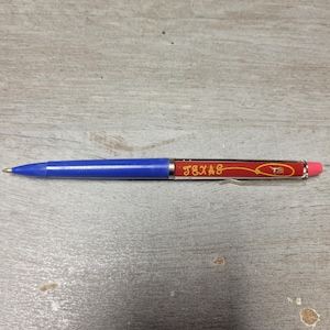Peut inclure: Un stylo à bille rétractable avec une pointe en plastique bleu et un corps rouge. Le corps affiche le mot TEXAS en lettres jaunes, un graphique de lasso jaune et une petite illustration de bœuf longhorn. Il possède un clip argenté et une gomme rose.