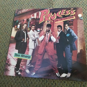 May include: A vinyl record cover featuring a group of five men in a street setting. The cover is titled "Process and the Doo Rags" with the album title "Too Sharp" printed below. The men are wearing stylish clothing from the 1980s.