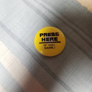 Può includere: Un bottone giallo con testo nero che dice "Press Here If You Dare!"