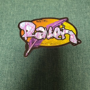 Może przedstawiać: Żółto-fioletowa naklejka z napisem "Raven" w stylizowanym foncie. Naklejka ma wzór czarnego pióra i tekst "WCW/nWo" oraz "1998 © "WCW" INC."
