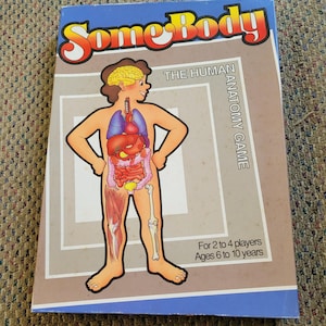 May include: A blue box for "Some Body, The Human Anatomy Game." The box features a cartoon illustration of a person with visible internal organs. Text on the box indicates it is for 2-4 players, ages 6-10.