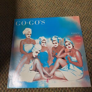 May include: Album cover for The Go-Go's "Beauty and the Beat." The cover features five women in white towels and face masks against a blue and pink background. The band's name is in white text at the top.