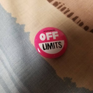 May include: A pink button with the text "OFF LIMITS" in white lettering.