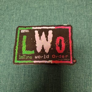 Könnte beinhalten: Ein schwarz-weißer Aufkleber mit dem Text "LWO Latino World Order" in einem grün-weiß-roten Farbschema. Der Aufkleber hat eine holografische Oberfläche.