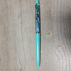 May include: A light blue ballpoint pen featuring a clear barrel section filled with liquid and floating graphics of black and white orcas. The lower barrel is solid light blue and displays the text OREGON COAST printed vertically in a dark blue font.