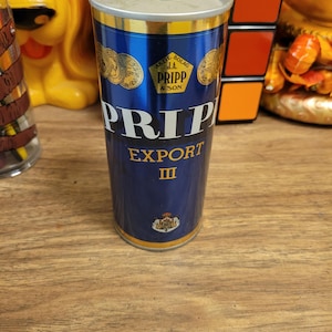May include: A vintage blue and gold beer can with the text "PRIPP EXPORT III". The can features gold accents, a gold rim, and a logo with the text "AKTIE J.A. BOLAG PRIPP & SON".