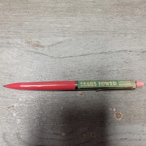 May include: A retractable ballpoint pen with a solid coral-colored lower barrel and a metallic gold upper barrel. The upper section features the green text SEARS TOWER CHICAGO ILLINOIS, a silver pocket clip, and a light pink eraser at the end.