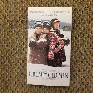 May include: A VHS tape cover featuring Jack Lemmon, Walter Matthau, and Ann-Margret in a snowy scene. The title of the movie is "Grumpy Old Men: A Fifty-Year Fight".