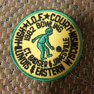 Op de afbeelding: Een geborduurde patch in geel en groen met de tekst "1982 I.O.F. COURT-NISM ILLINOIS & EASTERN BADGER & JAMESVILLE WISCONSIN BOWLING" en een cartoon van een persoon die bowlt.