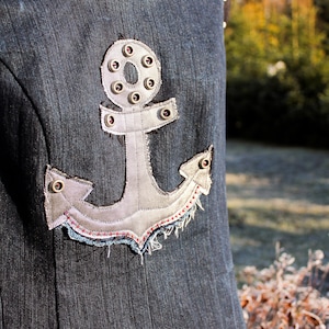 Könnte beinhalten: Ein Jeanskleid mit einem großen silbernen Anker-Applikationen. Der Anker ist mit kleinen silbernen Nieten verziert und hat einen Used-Look.