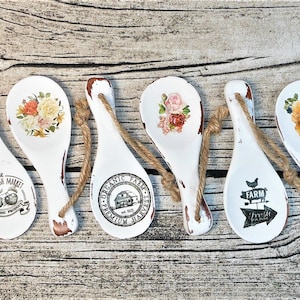 May include: Six white wooden spoons with twine hangers, each decorated with a different design. The designs include floral patterns, a farm fresh market logo, and a farm fresh produce logo.