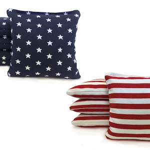 May include: Set of eight bean bags for cornhole games. Four bean bags are navy blue with white stars and four bean bags are red and white striped.