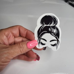 May include: A black and white sticker featuring a woman with her hair in a bun and her eyes closed. The sticker is on a white background.