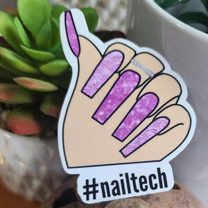May include: A sticker featuring a hand with long, purple nails. The nails have a mix of solid purple and patterned designs. A silver ring is on the ring finger. The text "#nailtech" is at the bottom of the sticker.