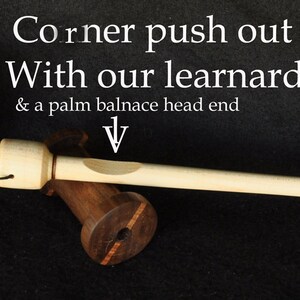 May include: A wooden corner push out tool with a learnard grip and a palm balance head end. The tool is light-colored with a long, slender handle. Several wooden spools with two-tone color blocking are also in the image.