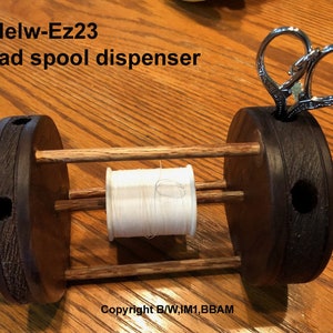May include: Wooden thread spool dispenser with a white thread spool and a pair of silver scissors. The dispenser has a label that reads "Modelw-Ez23 Thread spool dispenser".