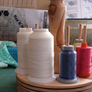 May include: A wooden thread stand with four spools of thread. Two spools are white, one is blue, and one is pink. The stand has a rotating base.