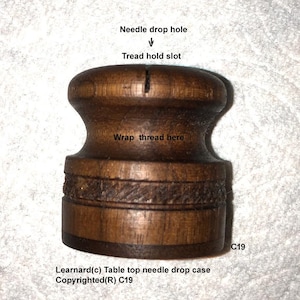 May include: A wooden needle drop case with a slot for holding thread and a hole for dropping needles. The case is labeled "Learnard(c) Table top needle drop case Copyrighted(R) C19".