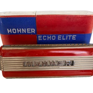 May include: A vintage red and silver Hohner Echo Elite harmonica with its original case. The harmonica has a red body with silver accents and the name "Hohner" is visible. The case is red and blue with the words "Hohner" and "Echo Elite".