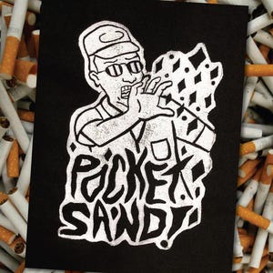 May include: Black and white illustration of a person wearing a hat and sunglasses, holding a large object with the text "PICKET SAND" in a distressed font.