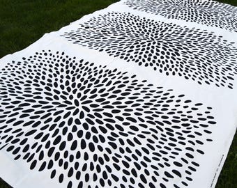 May include: White fabric with a repeating black pattern of stylized, oval shapes radiating from a central point. The design is spread across the fabric in three horizontal rows. The fabric is laid out on green grass.