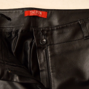 May include: Black leather pants with a zipper fly and button closure. The pants have a label that reads "TAIFUN COLLECTION".