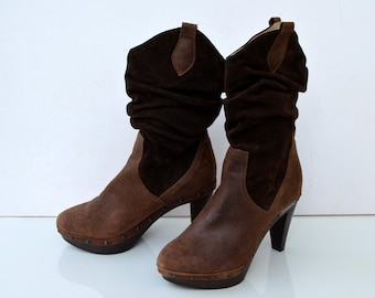 May include: A pair of brown suede heeled boots with a slouchy design. The boots have a pointed toe and a block heel.