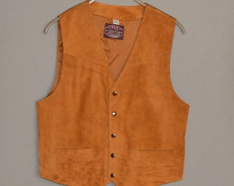 May include: A tan suede vest with a V-neck and a button-up front. The vest has two front pockets and is hanging on a metal hanger. The label inside the vest reads "John F Gee".